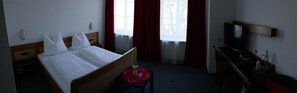 Een hotelkamer met een bed, een bureau, een stoel, een televisie en een raam met gordijnen.