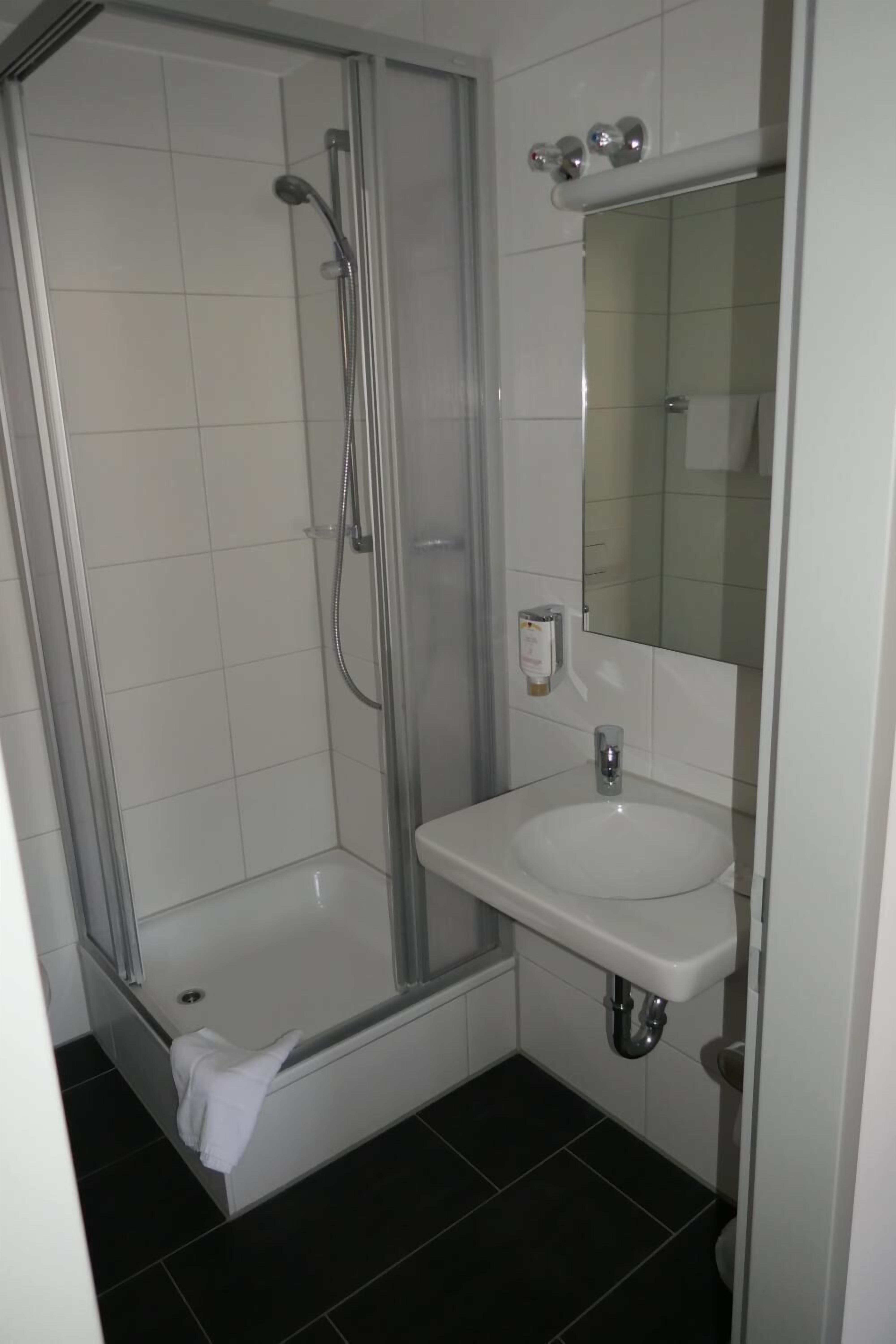 Ein Badezimmer mit einer Duschkabine, einem weißen Waschbecken und einem Spiegel darüber.