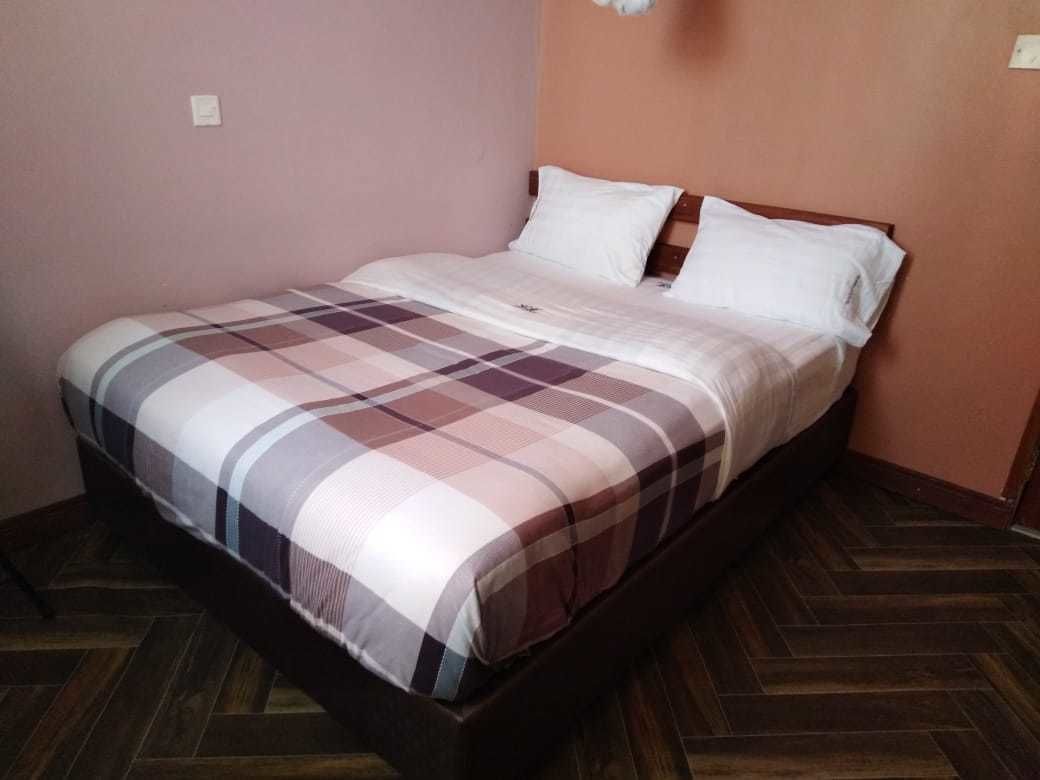 Una cama individual con colcha a cuadros, cabecero de madera y suelo de madera.