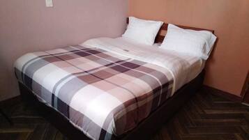 Una cama individual con colcha a cuadros, cabecero de madera y suelo de madera.