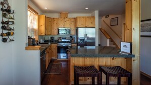 A kitchen with wooden cabinets, stainless steel appliances, and a built-in island with stools. - Luxurious, affordable condo one mile from downtown (Ketchum)