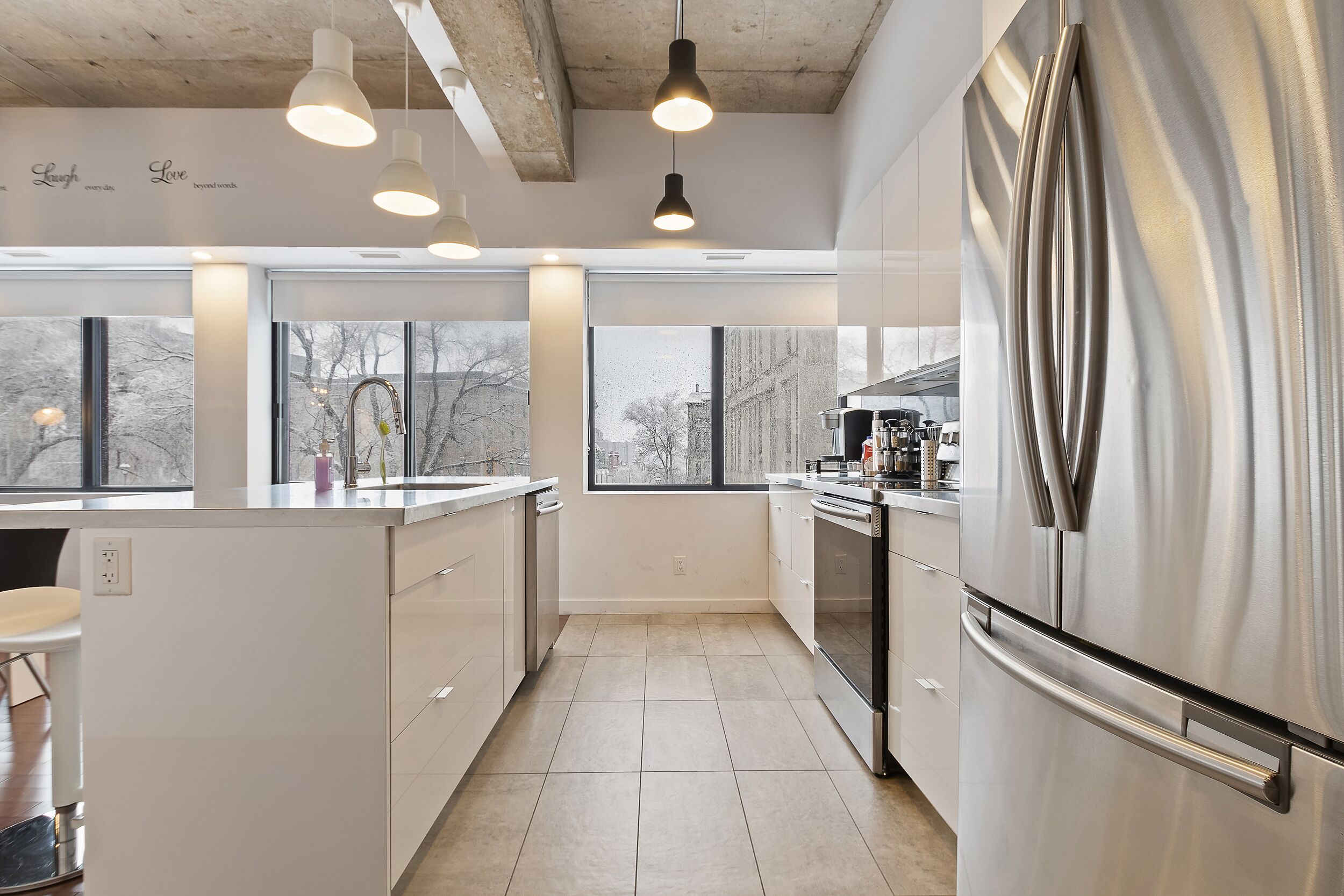 A modern kitchen with a stainless steel refrigerator, white cabinetry, and pendant lighting.
