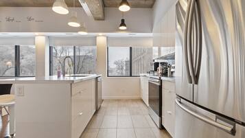 A modern kitchen with a stainless steel refrigerator, white cabinetry, and pendant lighting.
