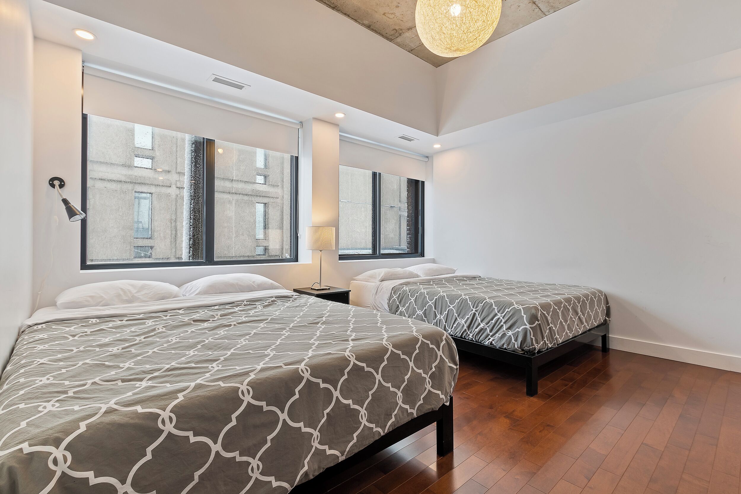 A modern hotel room with two beds, large windows, and a wooden floor.