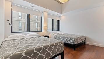 A modern hotel room with two beds, large windows, and a wooden floor.