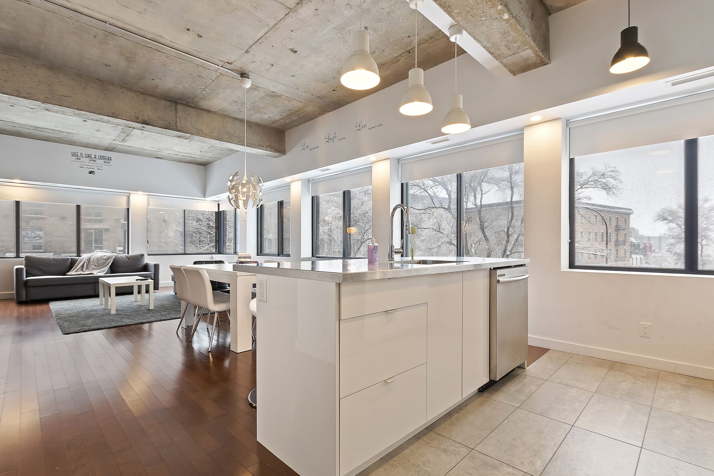 A modern kitchen with a central island, large windows, and a dining area with a sofa and chairs.