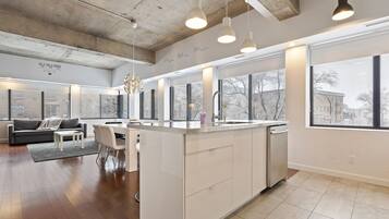 A modern kitchen with a central island, large windows, and a dining area with a sofa and chairs.