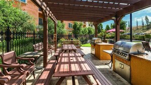 An outdoor patio with wooden benches and picnic tables, a barbecue grill, and a pergola structure. -  NAPAS GEM!  1 BEDROOM (Napa)