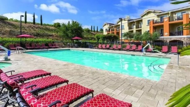 A swimming pool with red patterned lounge chairs and a building with balconies in the background. -  NAPAS GEM!  1 BEDROOM (Napa)