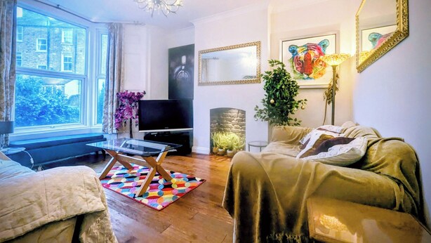 A living room with a sofa, a television, a chandelier, and a large window.