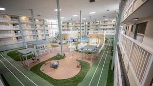 A multi-story hotel with balconies, a central courtyard with seating, and a pool area.