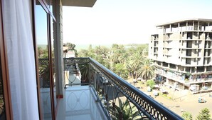 A balcony with a metal railing overlooking a street with palm trees and a building under construction. - Wynn Hotel - Bahir Dar (Bahir Dar)