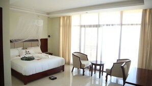 A hotel room with a large bed, a bedside table, a chair, a small table, and a window with curtains. - Wynn Hotel - Bahir Dar (Bahir Dar)