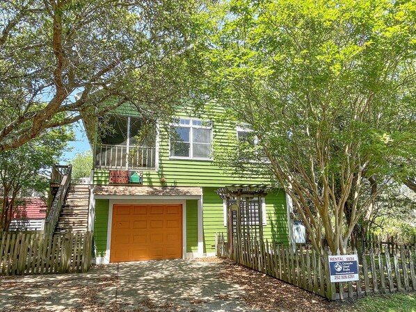 A two-story house with a green exterior, a wooden fence, and a garage.