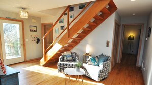 Amplia sala de estar con una escalera de madera, un conjunto de sofás, una mesa de centro y una puerta que da al exterior.