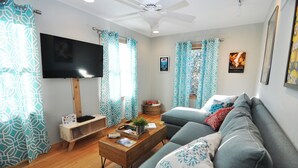 Una sala de estar con un sofá gris, una mesa de centro de madera, un televisor de pantalla plana y cortinas estampadas.