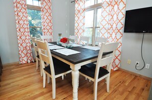 A dining area with a wooden table, white chairs, and a TV mounted on the wall.