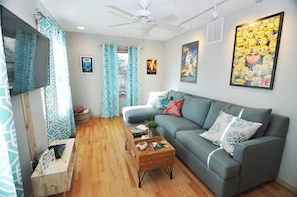A modern living room with a grey sofa, wooden coffee table, and patterned curtains.