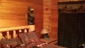 A wooden room with a bed, a nightstand, a lamp, and a bear sculpture on the wall. - LOG HOME CANINE RETREAT (Pyatt)