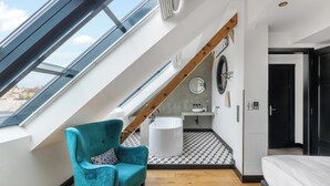 Un dormitorio estilo loft moderno con tragaluz, un ventanal grande, una viga de techo de madera, una bañera y piso de madera.
