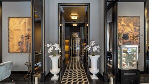 Un vestíbulo de hotel con suelo a cuadros, dos grandes jarrones blancos con flores, un refrigerador con comida y un cuadro grande en la pared.