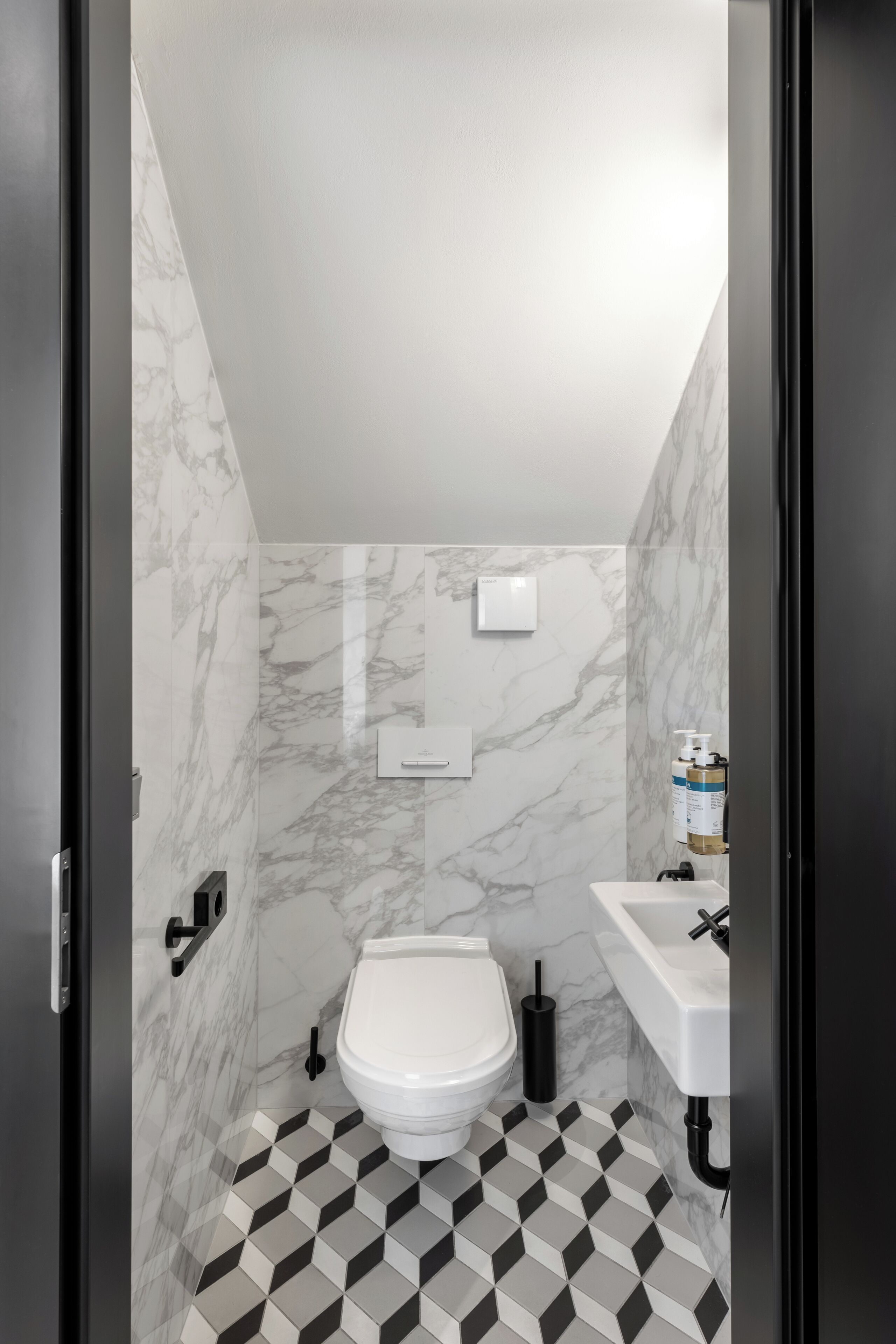 A bathroom with a white toilet, a sink, and a mirror. The walls have a marble pattern, and the floor has a black and white checkered tile design.