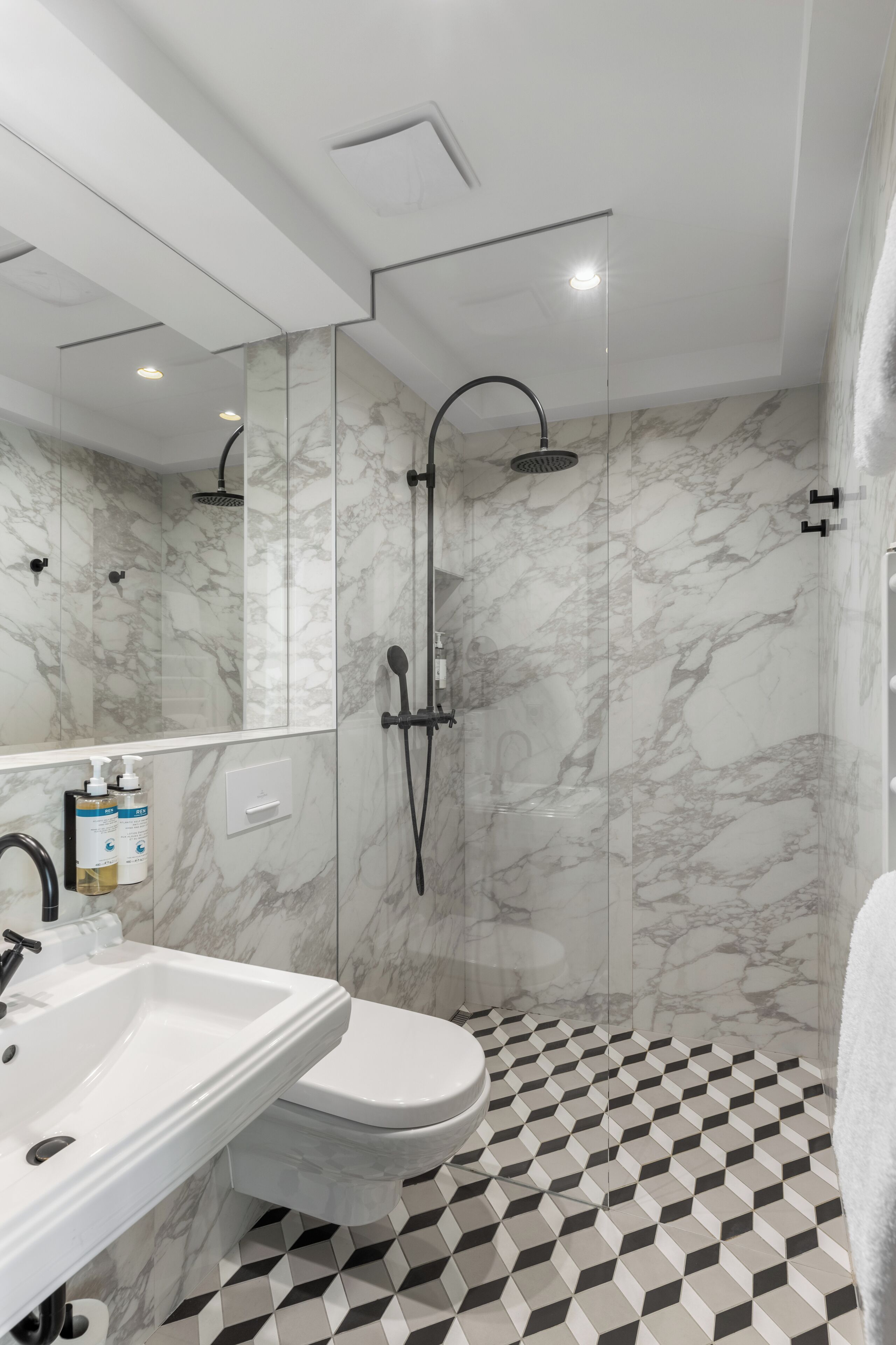 A modern bathroom with a marble shower, a white sink, and a toilet.
