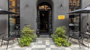 Entrada de un edificio con puerta negra, un letrero que dice "REPUBLICA" y área de estar al aire libre con sillas y sombrillas.