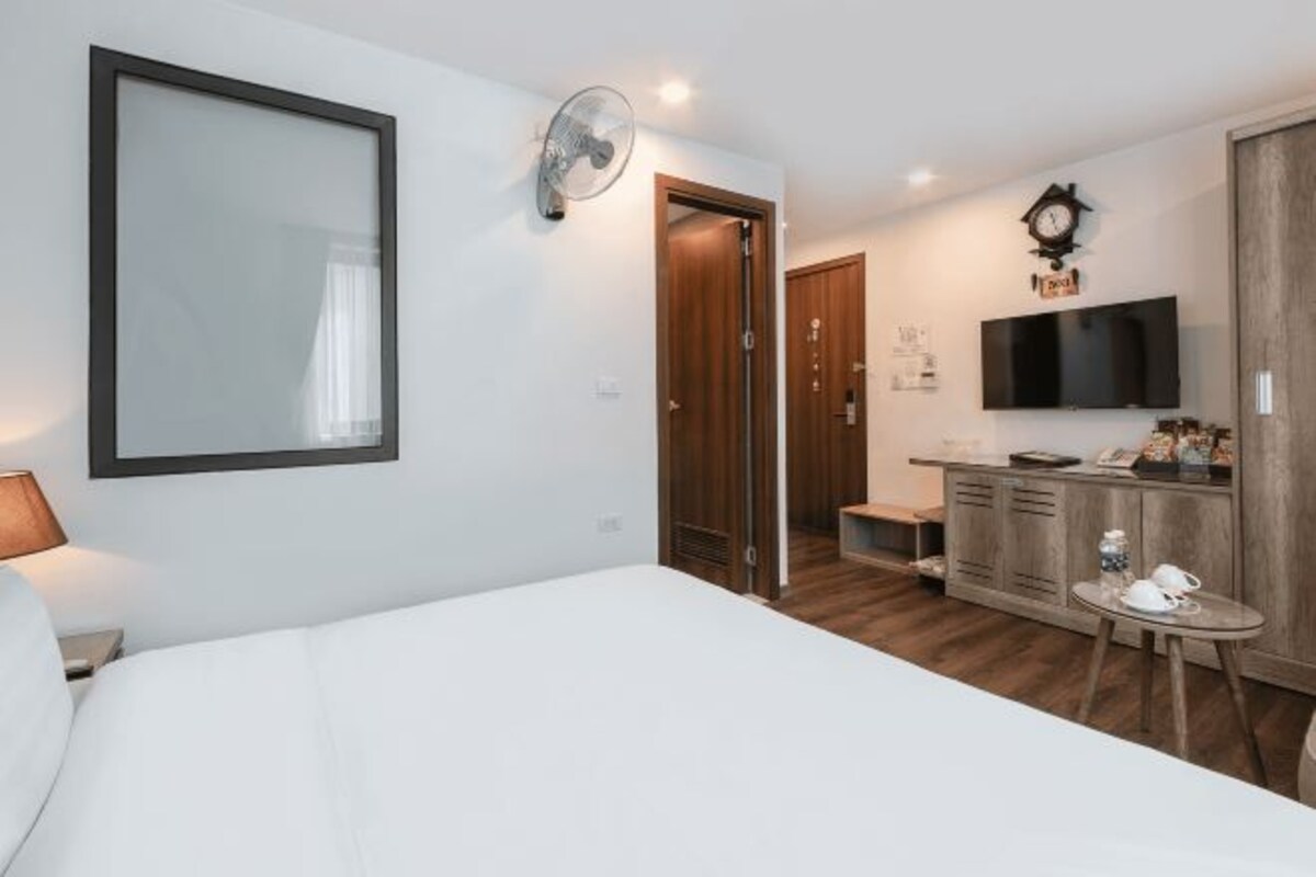 Une chambre d’hôtel comprenant un lit, une table de chevet, un téléviseur fixé au mur, une armoire en bois, une petite table avec des tasses et une porte donnant sur une salle de bain.