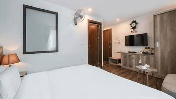 Habitación de hotel con cama, escritorio con televisor de pantalla plana, armario de madera, reloj y espejo.