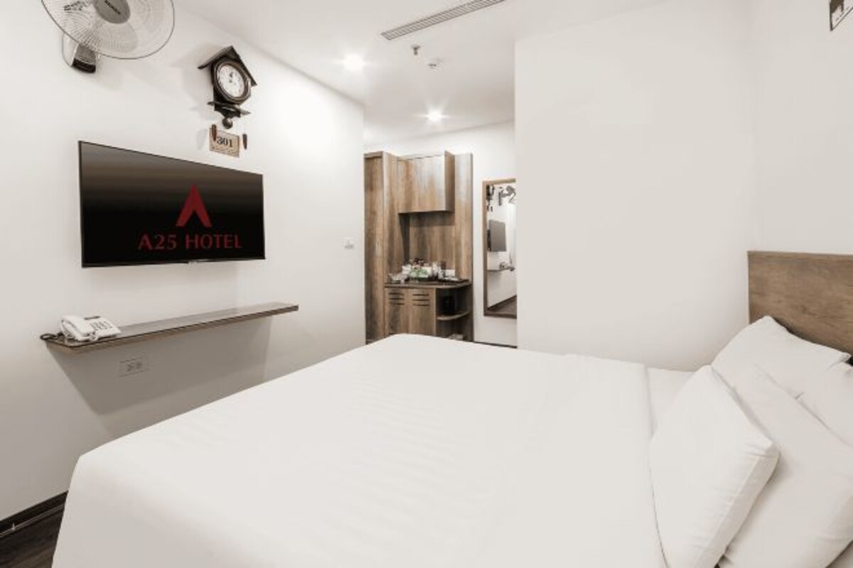 Une chambre d’hôtel avec un lit, un téléviseur fixé au mur, une horloge et une armoire en bois.