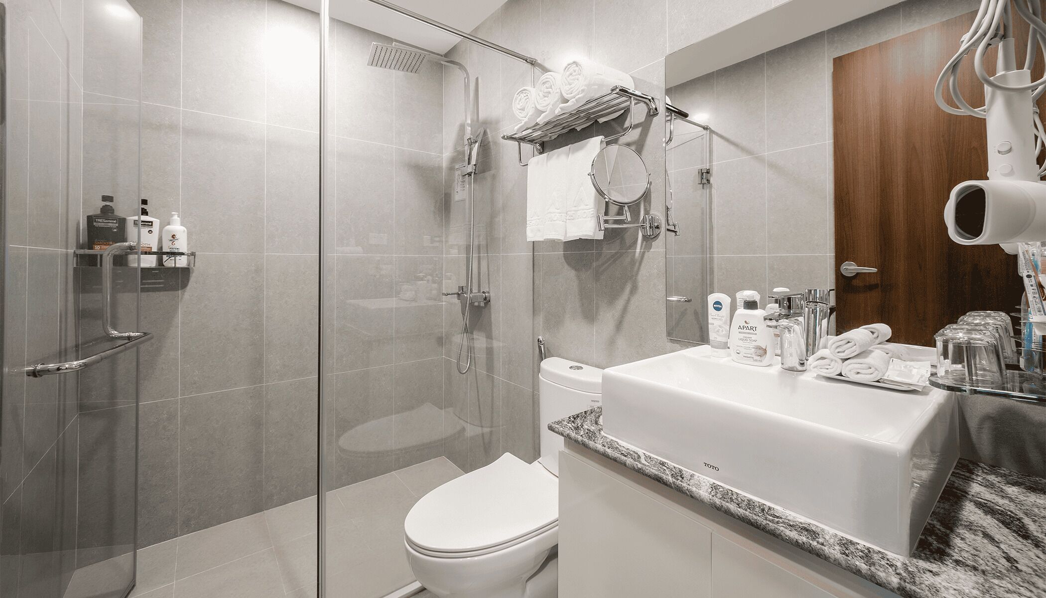 Une salle de bain moderne avec une douche à parois de verre, des toilettes blanches et un meuble-lavabo avec des articles de toilette.