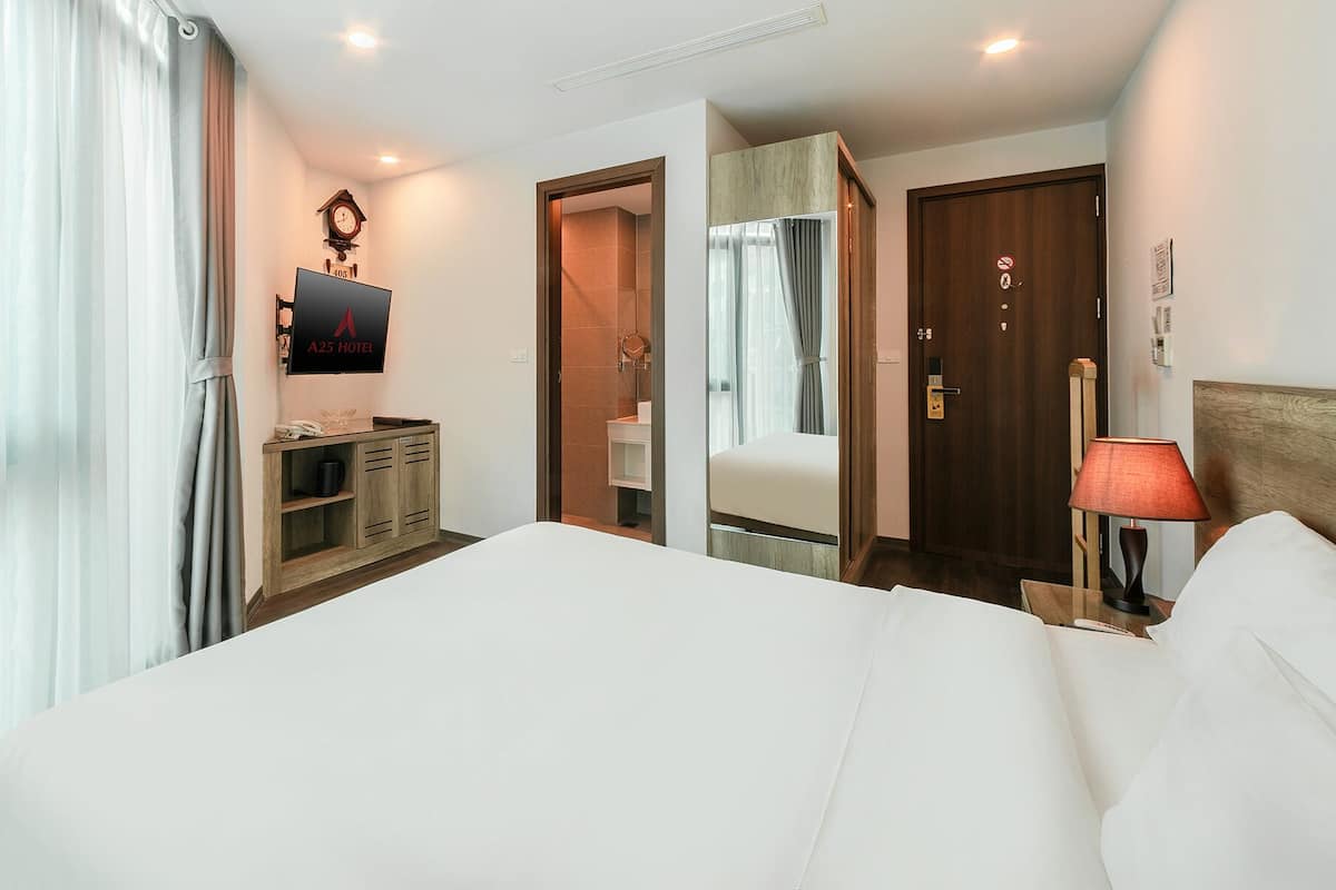 A hotel room with a large bed, a wooden dresser, a mirror, a clock, and a door with a sign.