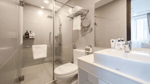 A modern bathroom with a glass-enclosed shower, a toilet, and a large sink with toiletries. - A25 Hotel - Hoang Dao Thuy 1 (Hanoi)
