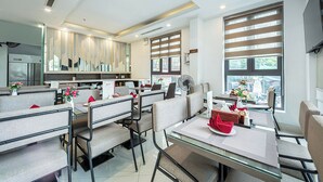 A modern dining area with booths and tables, large windows with blinds, and a kitchen area in the background. - A25 Hotel - Hoang Dao Thuy 1 (Hanoi)