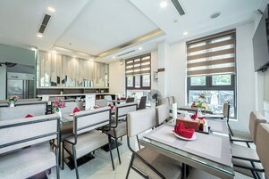 A modern dining area with booths and tables, large windows with blinds, and a kitchen area in the background.