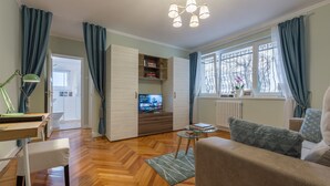 Ein modernes Wohnzimmer mit Holzdielen in Fischgrätmuster, einem Glastisch, einer Couch, einem Fernseher und einem Bücherregal.