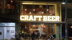 Eine Craft-Beer-Bar mit einer Neonreklame, Außenplätzen und einer sichtbaren Speisekarte.