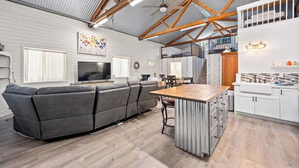 Een ruime woonkamer met een grote grijze modulaire bank, een houten eettafel en een keuken met witte kastjes en een houten aanrecht.