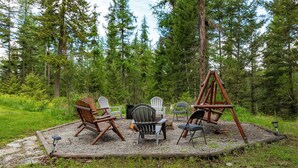Een rustieke buitenruimte met Adirondack stoelen en een schommel, gelegen in een grindcirkel omringd door een bosrijk gebied.