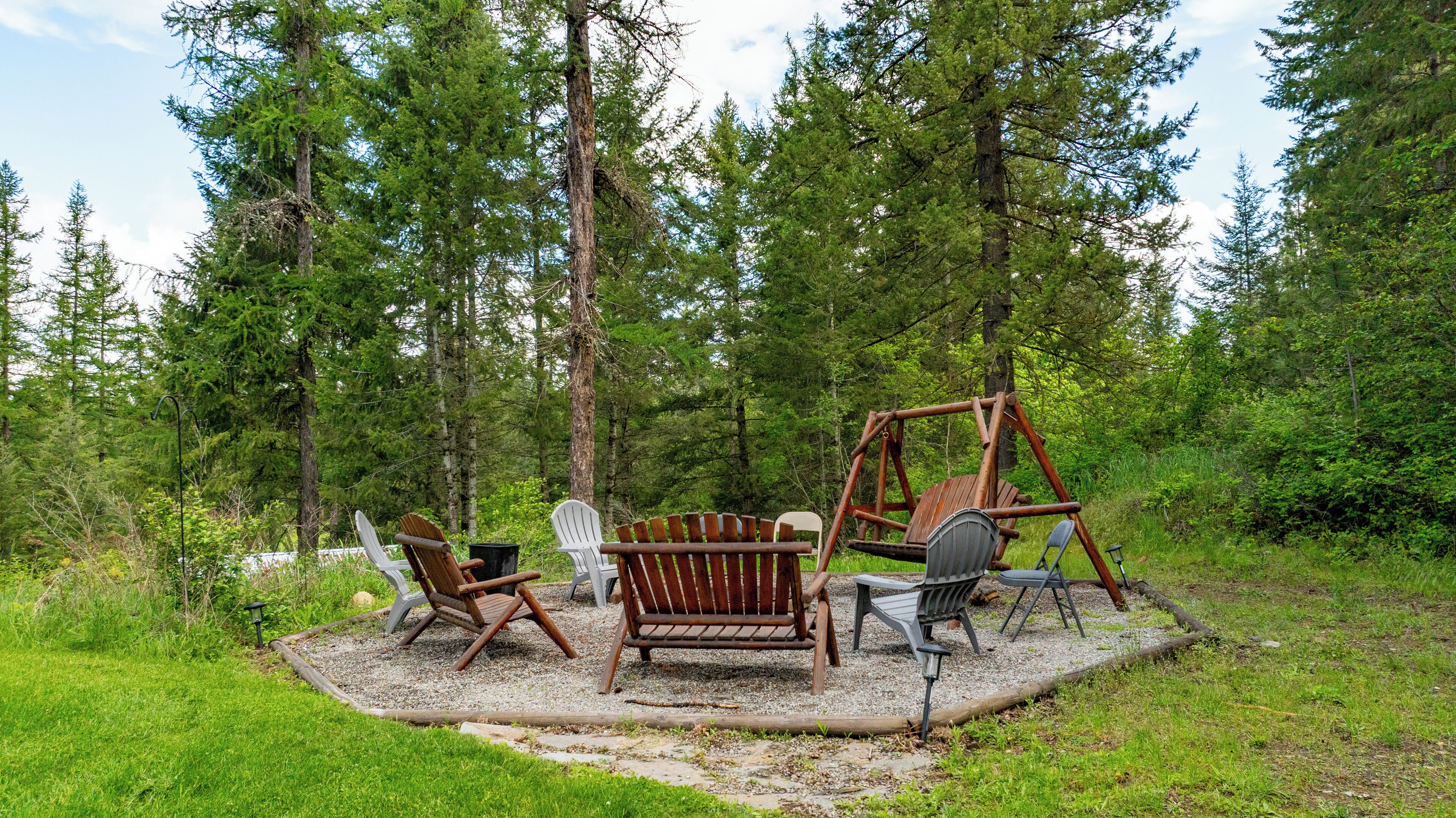 An outdoor seating area with wooden chairs and a swing set surrounded by trees.