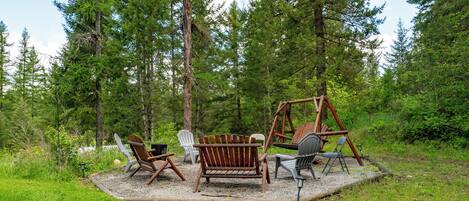 An outdoor seating area with wooden chairs and a swing set surrounded by trees.