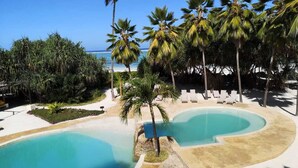 A resort pool area with palm trees, lounge chairs, and a clear view of the ocean.