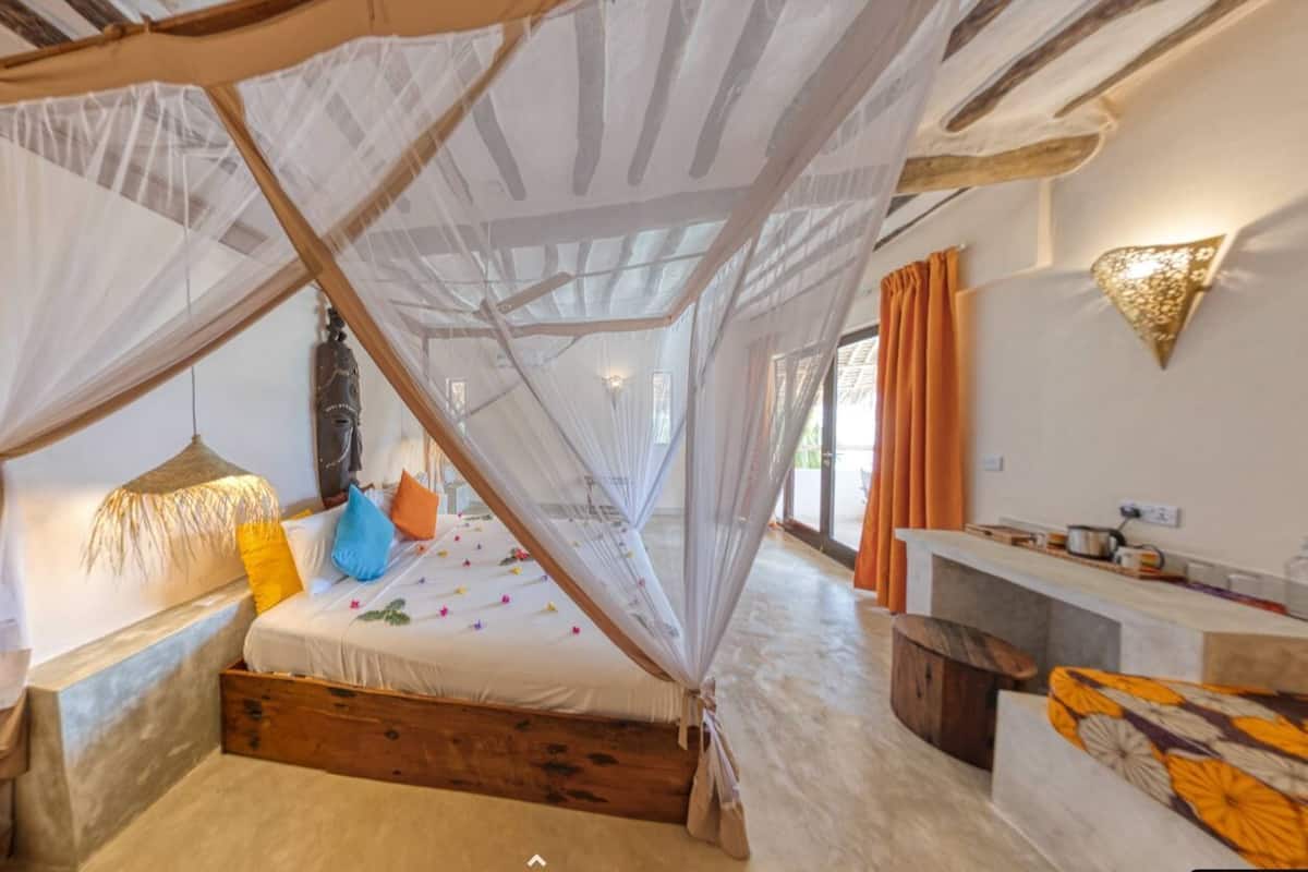 A bedroom with a canopy bed, a wooden bench, a small table, and a wall-mounted light fixture.