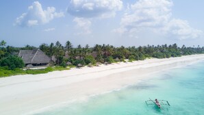 A beach with clear turquoise waters, a row of thatched-roof huts, and a row of palm trees.
