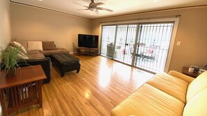 Un salon spacieux avec un grand canapé, un téléviseur posé sur un meuble en bois et un ventilateur de plafond.