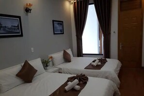 A hotel room with two beds, a nightstand, a small table, and a window with curtains.