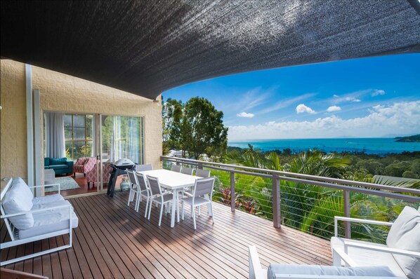 A balcony with a view of the ocean, a dining table, and seating. - The Power House - Views & More (Airlie Beach)