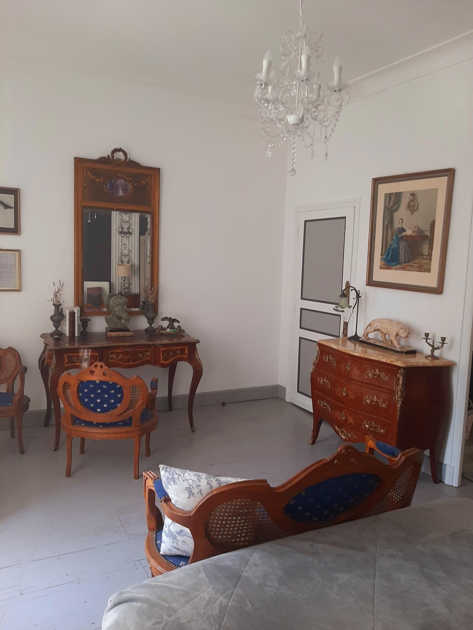 Une pièce comprenant un bureau en bois, une chaise, un canapé, un grand miroir, une commode et un lustre.