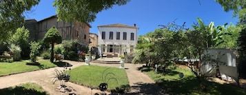 Un patio con una fuente central, rodeado de exuberante follaje y un edificio blanco con tejado de tejas.